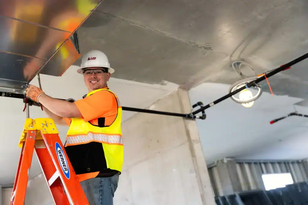 A Lee Company technician uses safety to climb a ladder and check plumbing.