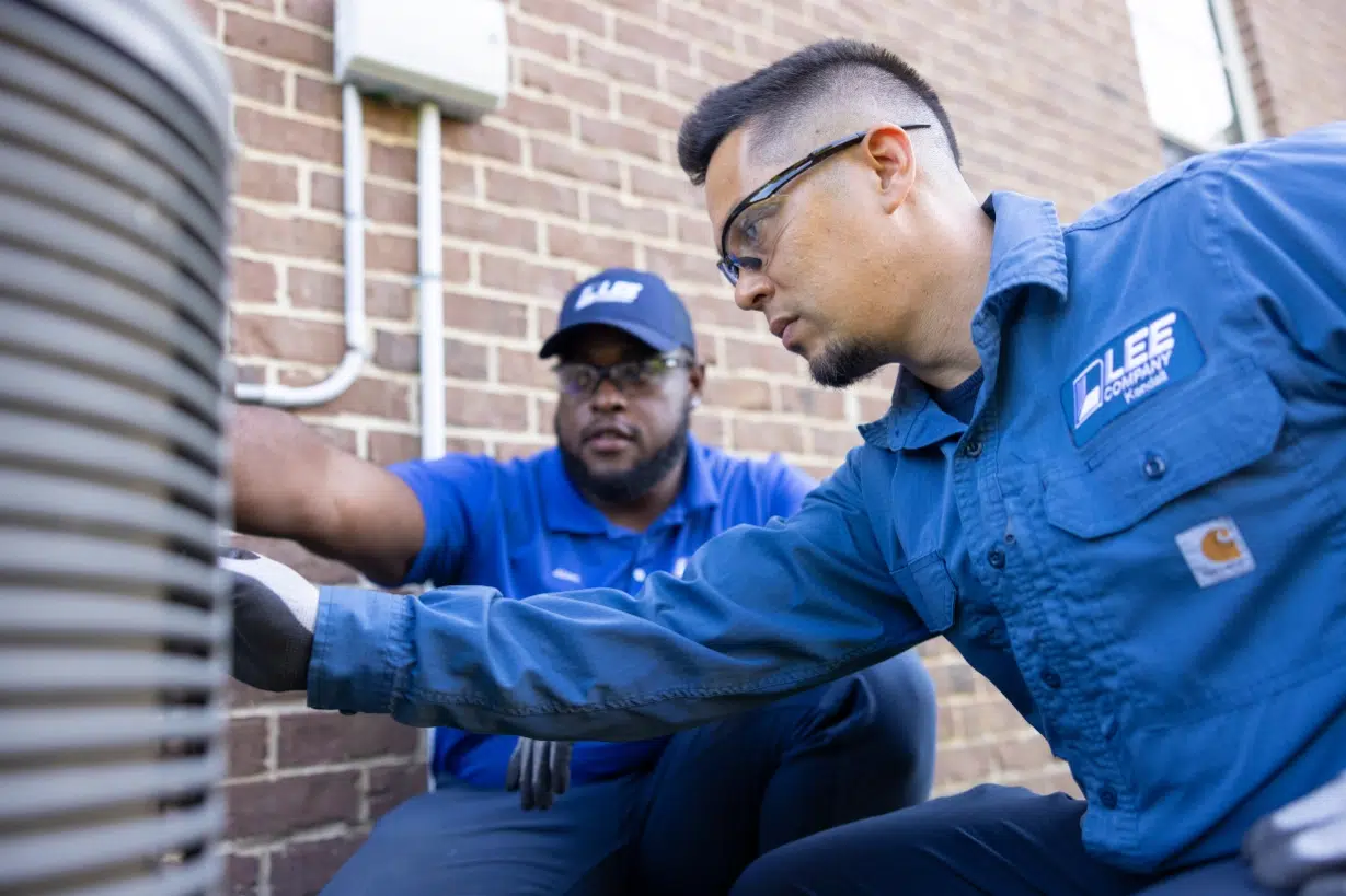Two Lee Company technicians looking at an outdoor HVAC system deciding whether they should repair or replace it.